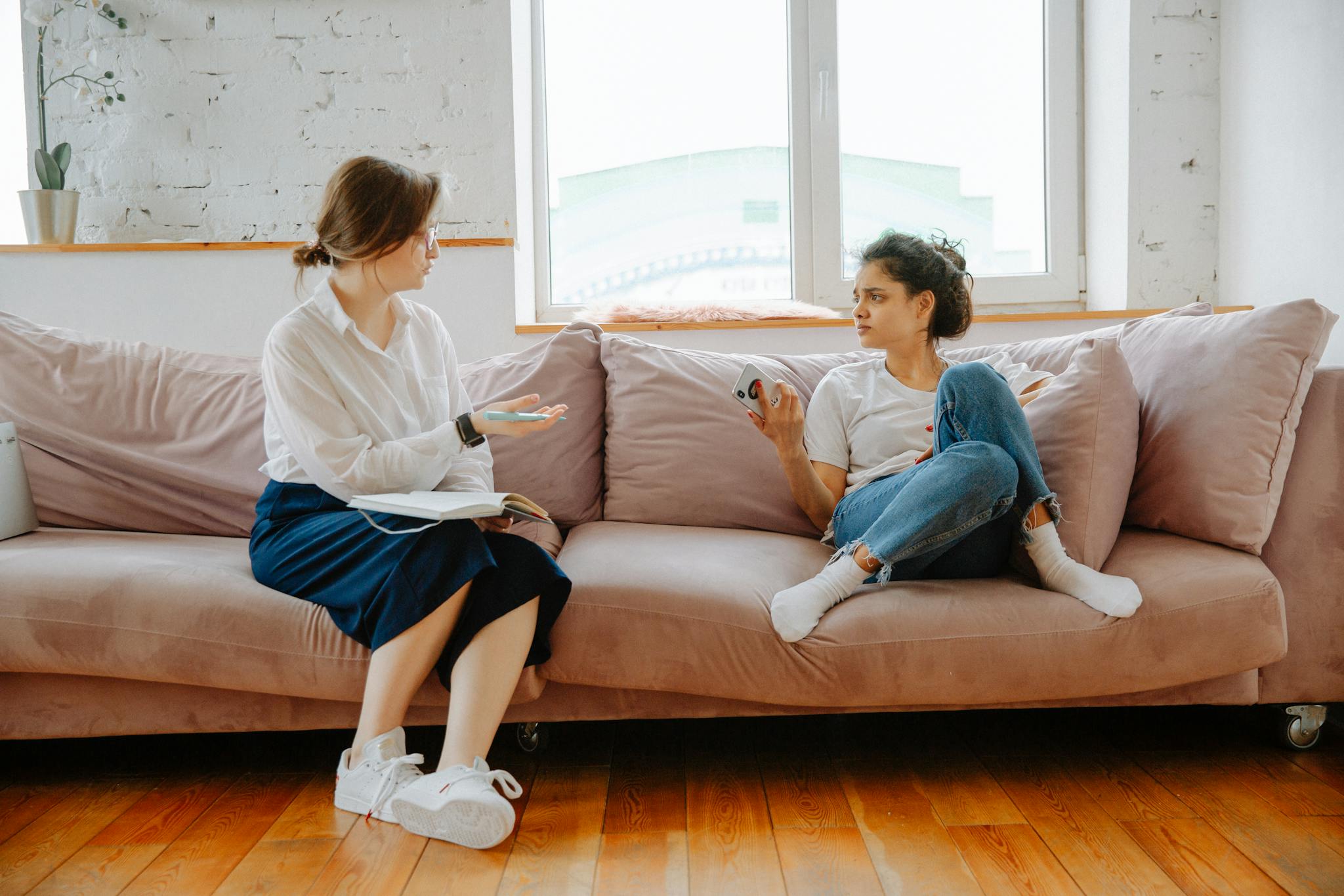 Two women engaging in a therapy session, discussing issues indoors on a couch.